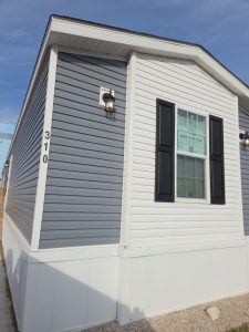 Manufactured home with blue and white siding, black shutters, and house number 310 by the corner.