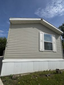 Light gray mobile home with white trim and shutters, single window, house number 319, and blue sky above.